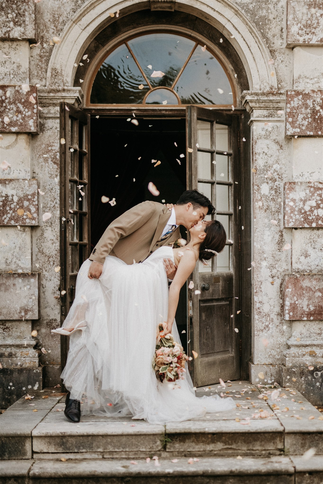 Dip kiss in stone doorway with rose petal confetti